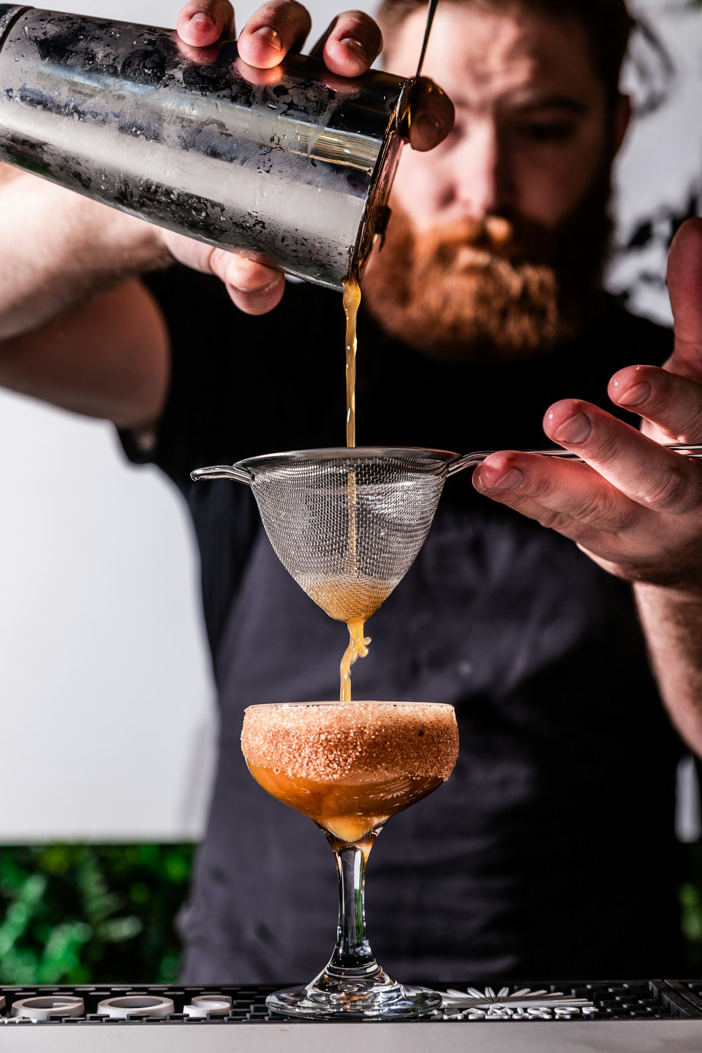 Bartender straining a freshly made cocktail into a coupe