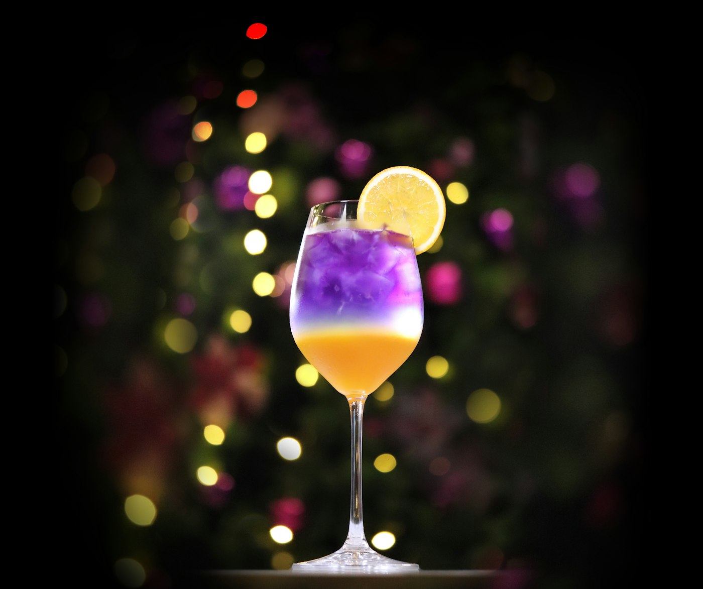 Layered signature cocktail against warm string-light bokeh